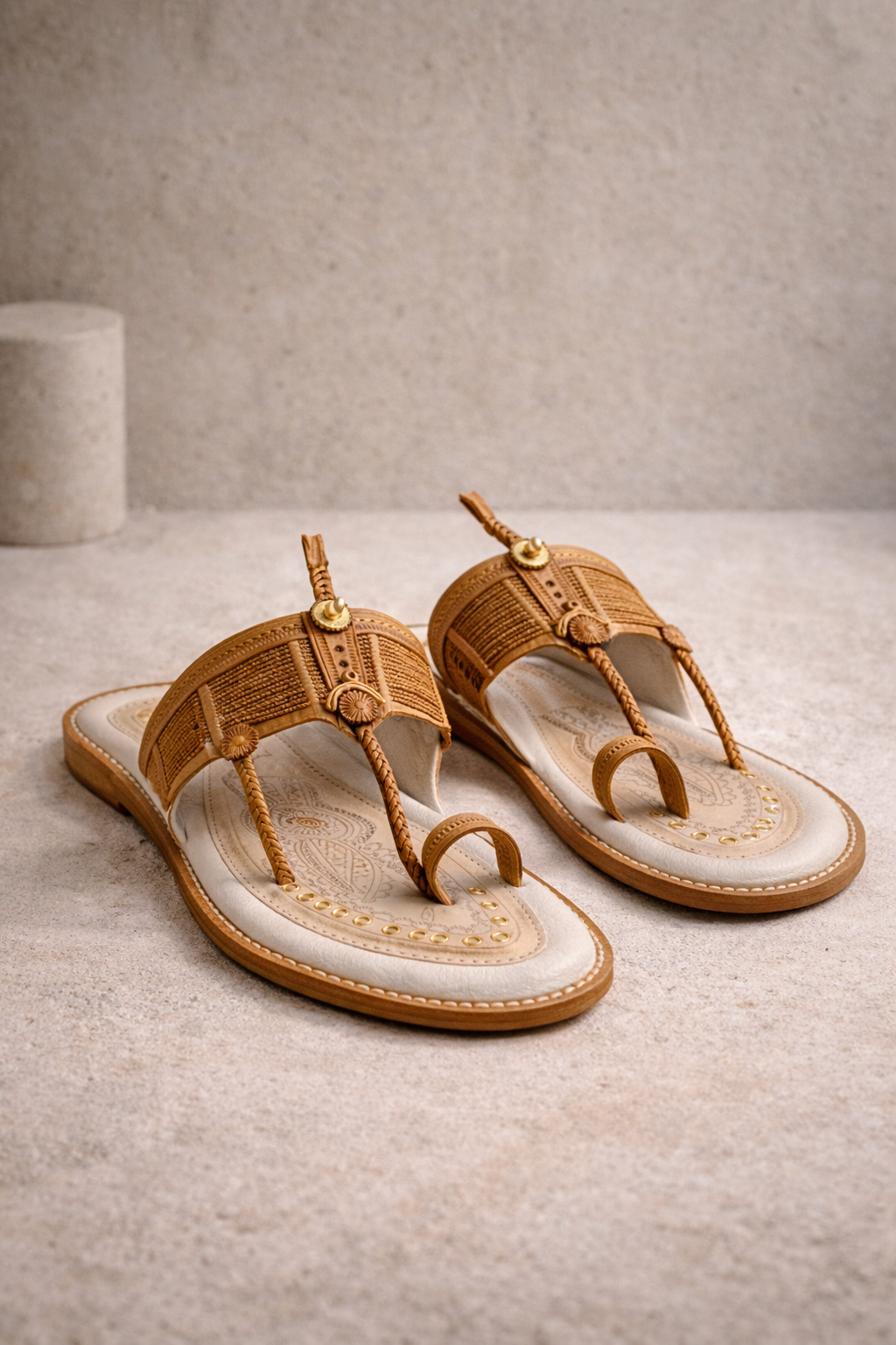 Handcrafted Kolhapuri leather chappals in natural tan, photographed on a neutral concrete background with studio lighting.